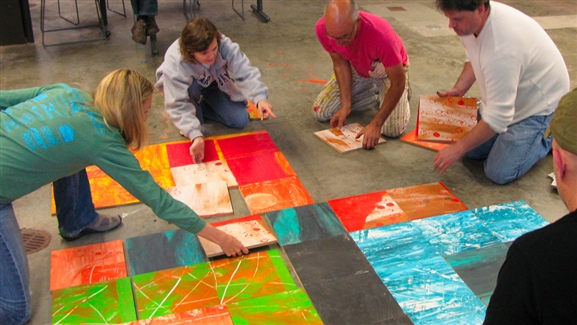 Four people placing large colored tiles on the ground