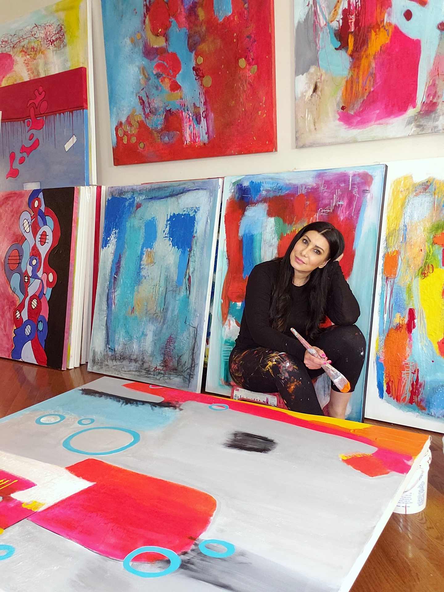 Artist Hiba Alyawer poses in front of brightly colored canvases in a studio